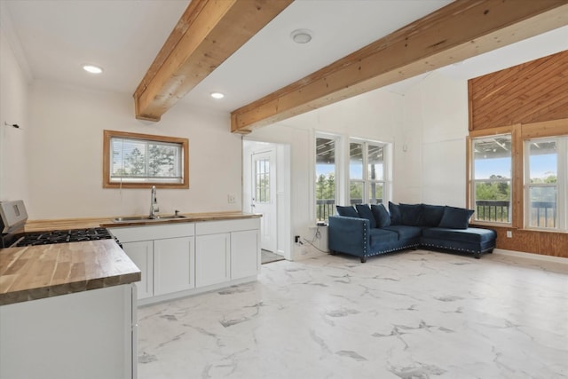 kitchen featuring wooden counters, a sink, beam ceiling, white cabinetry, and gas range