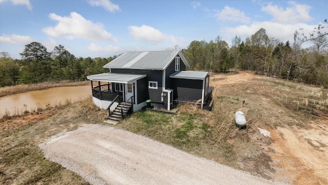 view of front facade with driveway, metal roof, and a view of trees
