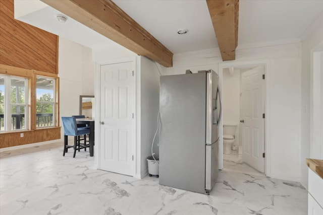 interior space featuring wood walls, stainless steel fridge, marble finish floor, and beam ceiling