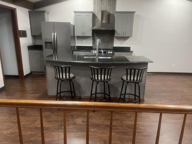 kitchen with wall chimney exhaust hood, dark wood-style flooring, an island with sink, and a sink