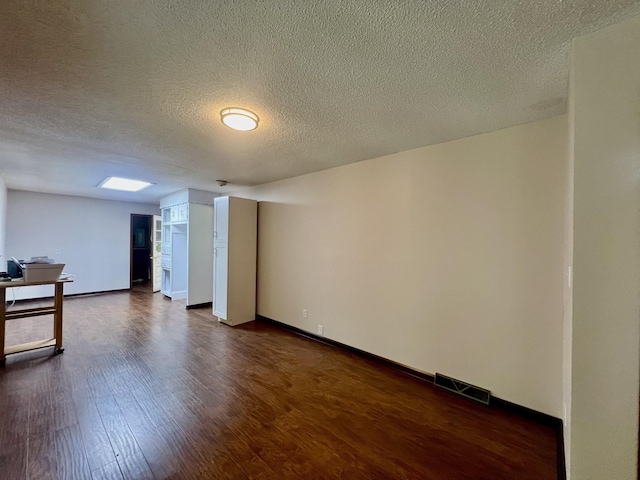 below grade area with baseboards, dark wood-style flooring, visible vents, and a textured ceiling