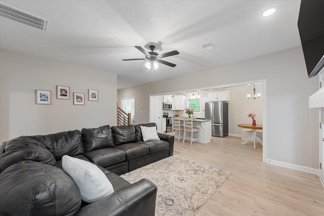 living room with stairway, light wood finished floors, a ceiling fan, baseboards, and a textured ceiling