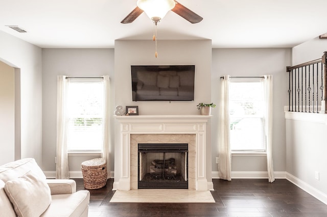 living area with dark wood finished floors, plenty of natural light, a premium fireplace, and ceiling fan