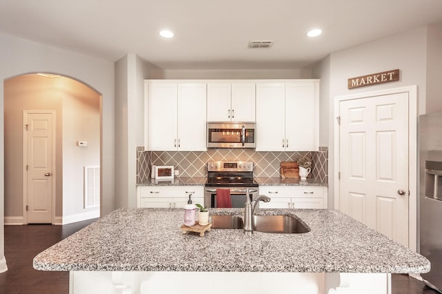 kitchen with light stone countertops, visible vents, a sink, arched walkways, and stainless steel appliances