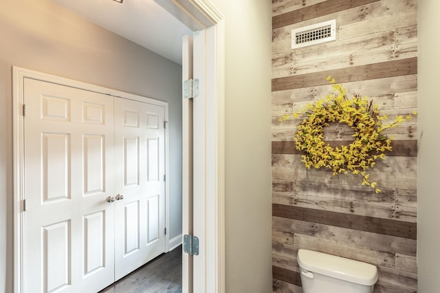 bathroom featuring toilet, wood walls, wood finished floors, and visible vents