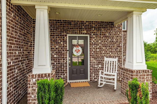 doorway to property with a porch and brick siding