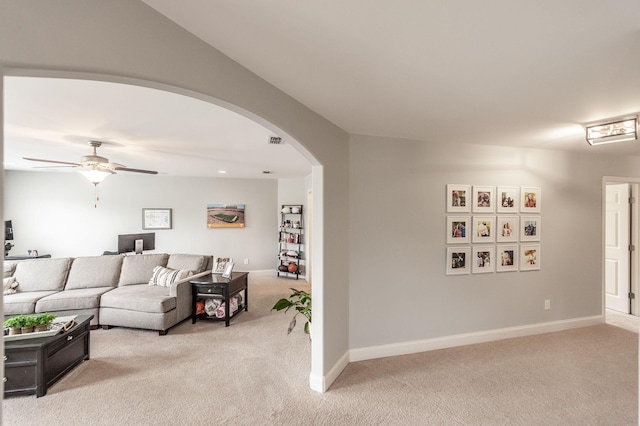 living area with arched walkways, visible vents, ceiling fan, and light colored carpet