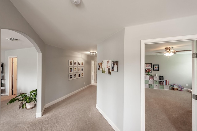 corridor with arched walkways, baseboards, visible vents, and light colored carpet