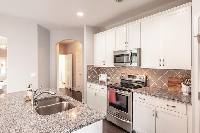 kitchen featuring a sink, white cabinetry, light stone countertops, arched walkways, and appliances with stainless steel finishes