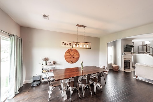 dining area featuring a fireplace with flush hearth, visible vents, baseboards, dark wood-type flooring, and arched walkways