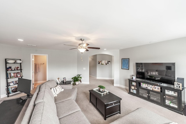 living room featuring light carpet, baseboards, a ceiling fan, and arched walkways