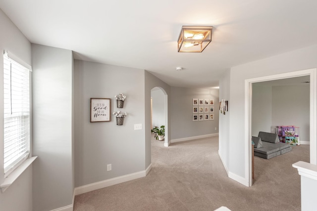 hall featuring light colored carpet, arched walkways, baseboards, and a healthy amount of sunlight