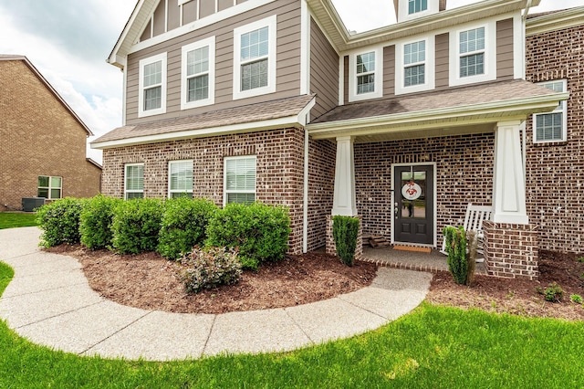 property entrance featuring a shingled roof, brick siding, and central AC