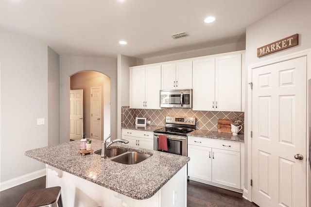 kitchen featuring a sink, stainless steel appliances, arched walkways, dark wood-style floors, and decorative backsplash