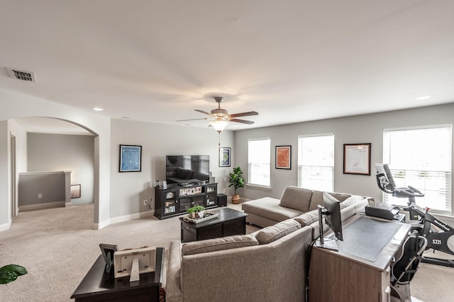 carpeted living area featuring arched walkways, ceiling fan, baseboards, and visible vents