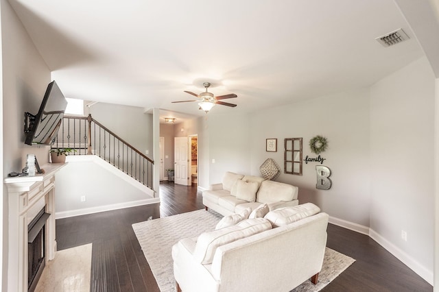 living room with a ceiling fan, baseboards, a fireplace with flush hearth, stairway, and dark wood-style floors