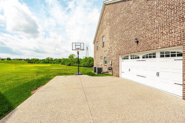 view of side of home with a garage, cooling unit, a lawn, brick siding, and driveway