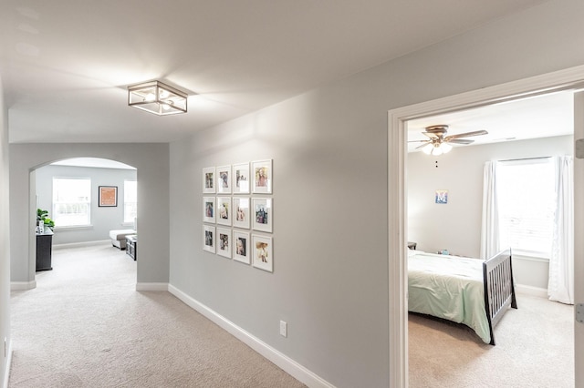 hallway with carpet flooring, arched walkways, and baseboards