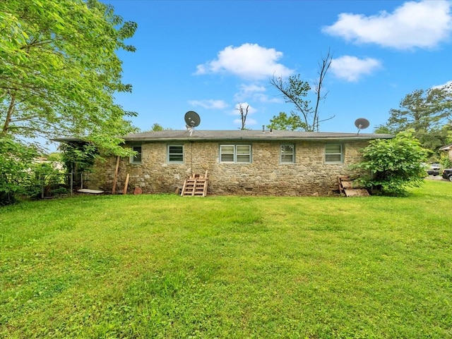 back of house featuring stone siding and a yard