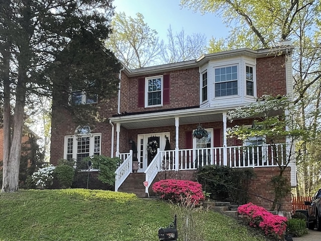 view of front of house featuring brick siding, a front yard, and a porch