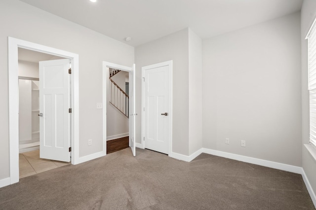 unfurnished bedroom featuring ensuite bath, carpet floors, and baseboards
