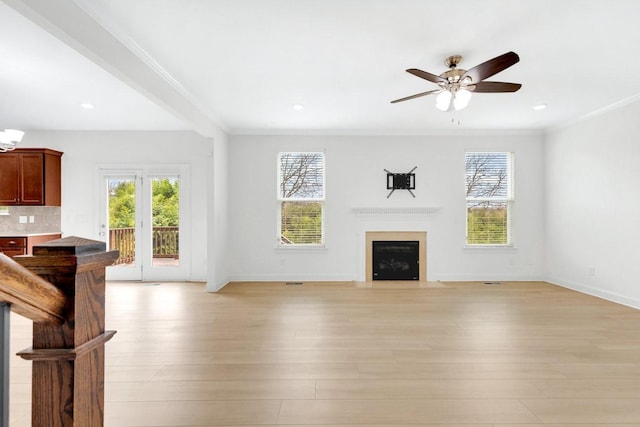 unfurnished living room with ornamental molding, a healthy amount of sunlight, ceiling fan, and a fireplace with flush hearth