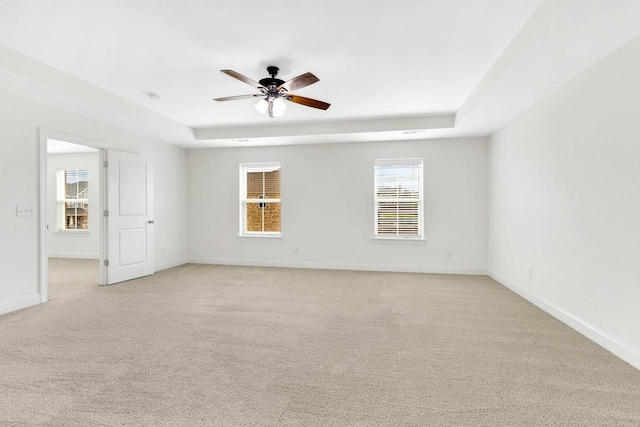 unfurnished room featuring light colored carpet, a ceiling fan, baseboards, and a raised ceiling