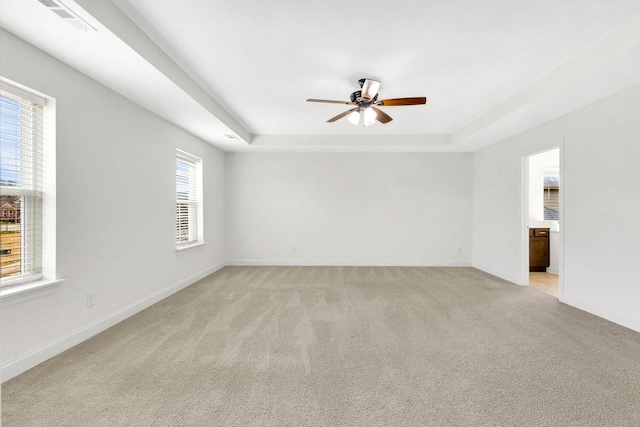 spare room with a tray ceiling, light carpet, baseboards, and ceiling fan