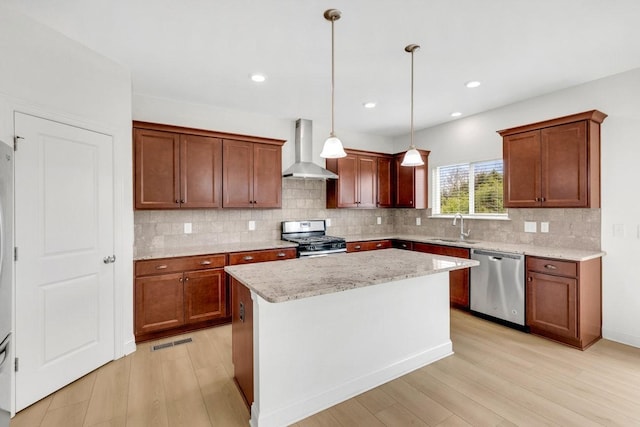 kitchen featuring a sink, decorative backsplash, wall chimney range hood, stainless steel appliances, and light wood-type flooring