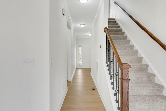 corridor featuring light wood finished floors, crown molding, stairway, baseboards, and visible vents