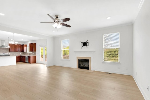 unfurnished living room featuring light wood-style flooring, visible vents, ceiling fan with notable chandelier, a fireplace with flush hearth, and crown molding