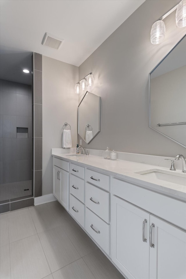 bathroom with a sink, double vanity, tiled shower, and visible vents