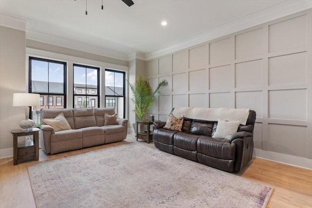 living room with baseboards, ceiling fan, a decorative wall, crown molding, and light wood-type flooring