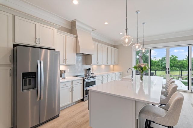 kitchen featuring a sink, a center island with sink, crown molding, light countertops, and appliances with stainless steel finishes