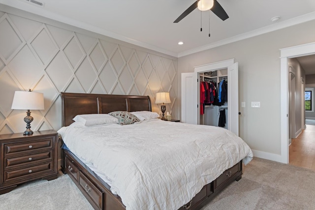 bedroom with a decorative wall, crown molding, light carpet, a walk in closet, and baseboards