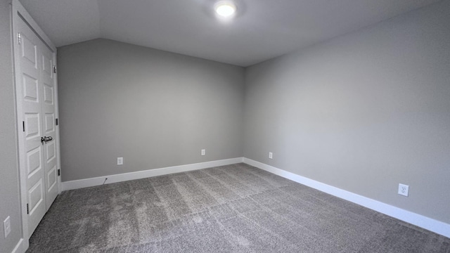 carpeted spare room featuring baseboards and vaulted ceiling