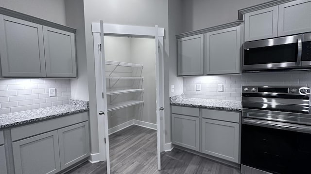 kitchen with dark wood-style flooring, backsplash, gray cabinetry, appliances with stainless steel finishes, and light stone counters