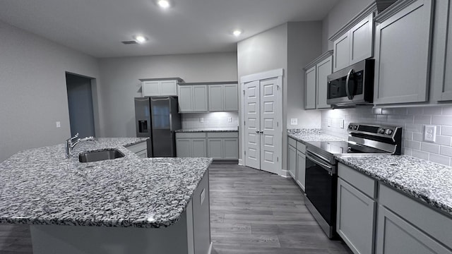 kitchen with a sink, dark wood-style flooring, decorative backsplash, light stone countertops, and appliances with stainless steel finishes