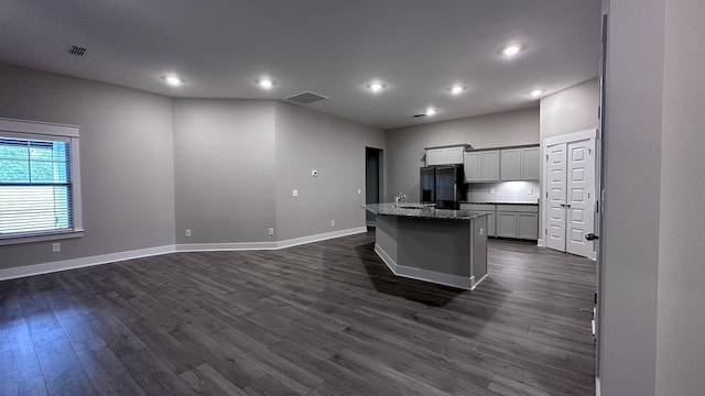 kitchen featuring black refrigerator with ice dispenser, dark wood finished floors, visible vents, a center island with sink, and baseboards