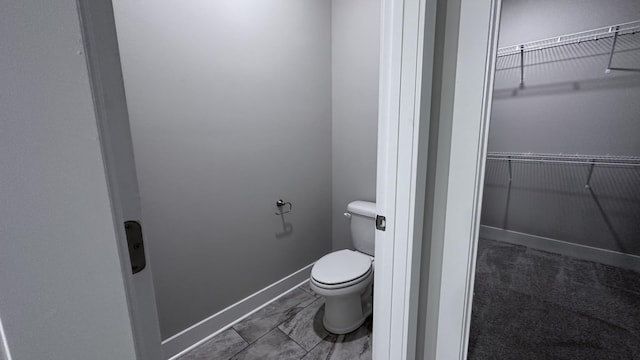 bathroom featuring a walk in closet, toilet, and baseboards