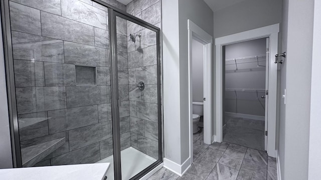 full bath featuring toilet, a stall shower, a walk in closet, baseboards, and marble finish floor