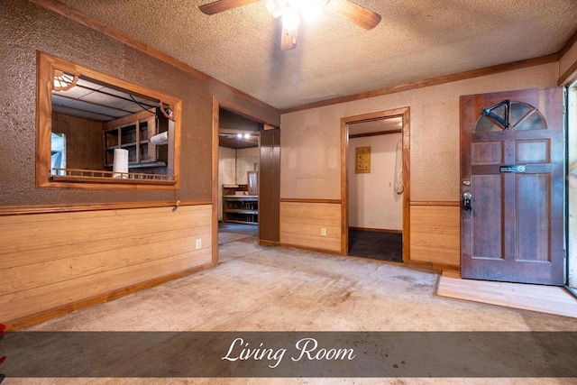 empty room with wood walls, a wainscoted wall, a textured ceiling, ceiling fan, and a textured wall