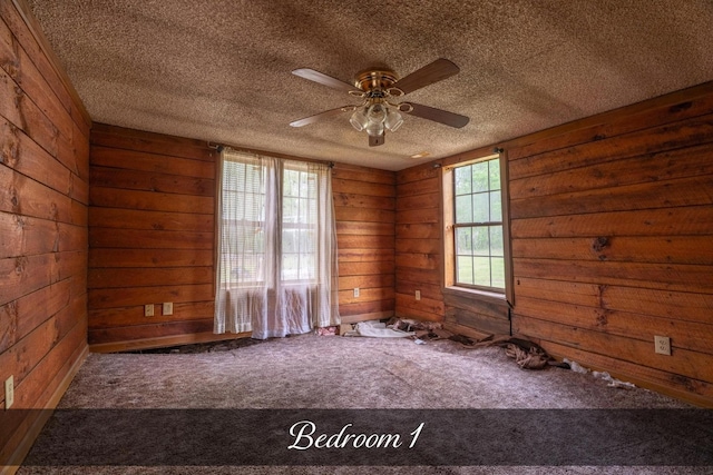 empty room with carpet flooring, wooden walls, ceiling fan, and a textured ceiling