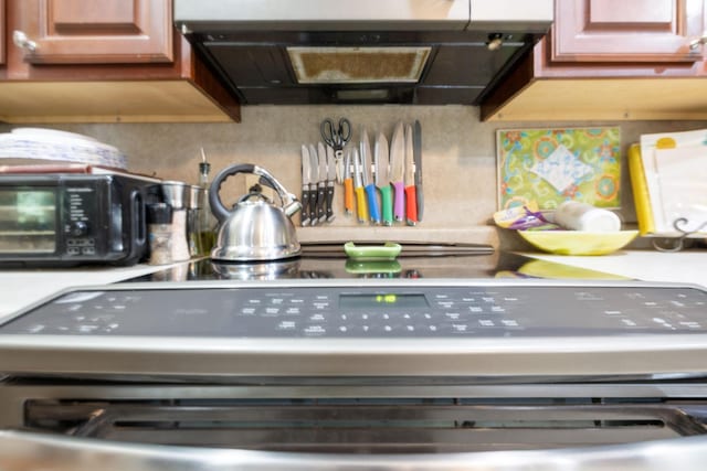 room details featuring range, ventilation hood, backsplash, light countertops, and black microwave