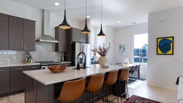 kitchen with a kitchen bar, a sink, wall chimney exhaust hood, light countertops, and tasteful backsplash