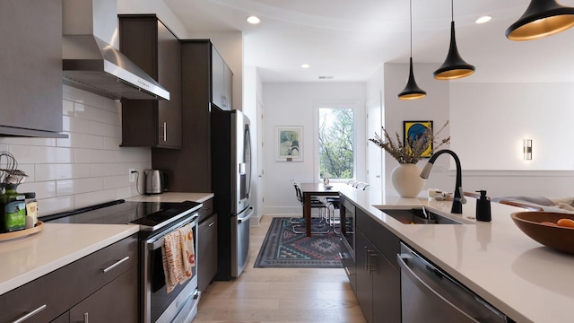 kitchen with dark brown cabinets, a sink, wall chimney exhaust hood, light countertops, and appliances with stainless steel finishes