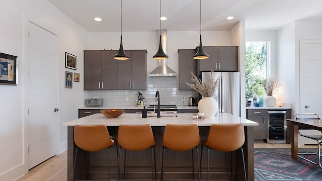 kitchen with tasteful backsplash, freestanding refrigerator, wall chimney exhaust hood, light countertops, and beverage cooler