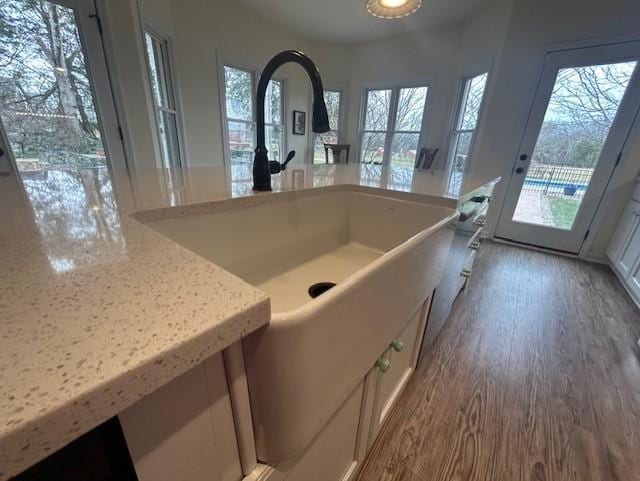 kitchen featuring white cabinetry, light stone countertops, a sink, and wood finished floors