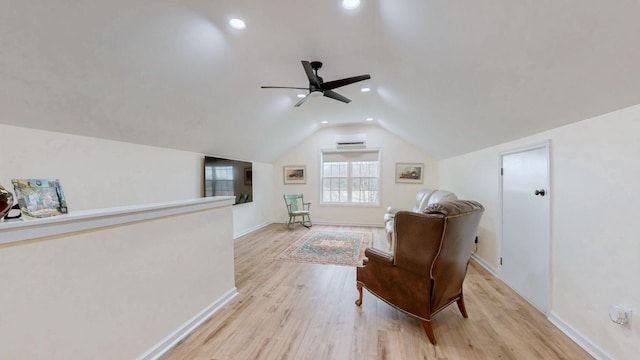 sitting room with a ceiling fan, light wood-style flooring, a wall unit AC, baseboards, and vaulted ceiling