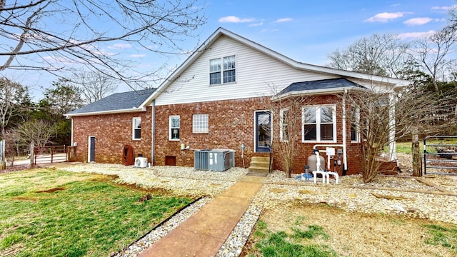 rear view of property featuring a gate, fence, central AC, and brick siding